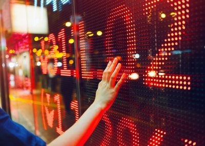 Woman's hand on stock exchange market display screen board on the street showing stock drops in red colour.