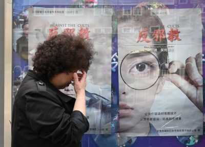 A woman walks past anti-cult posters beside a sidewalk in Beijing on April 23, 2019. 